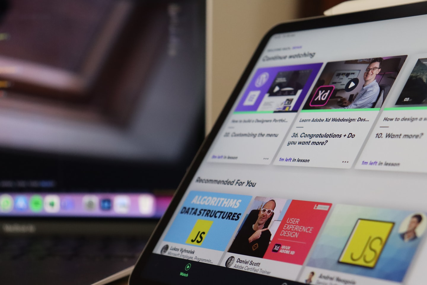 Na tablecie wyświetla się platforma e-learningowa z miniaturkami kursów.